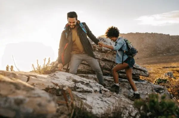 A man helping his partner over a rock during a hike