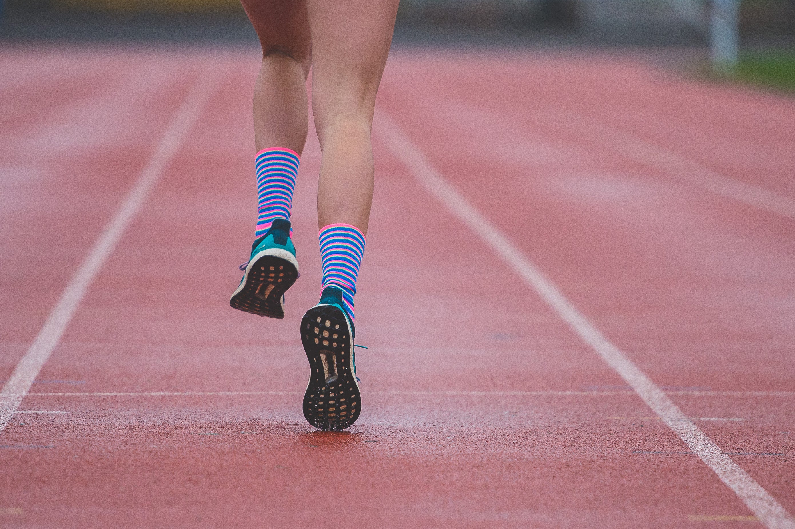 A woman running down a running track wearing striped socks.